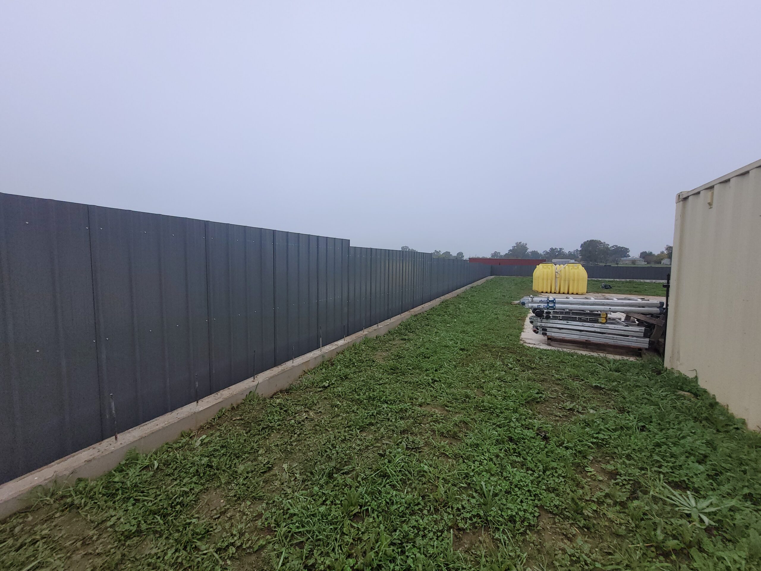 Corrugated metal fence running behind an existing concrete retaining wall, Elverta
