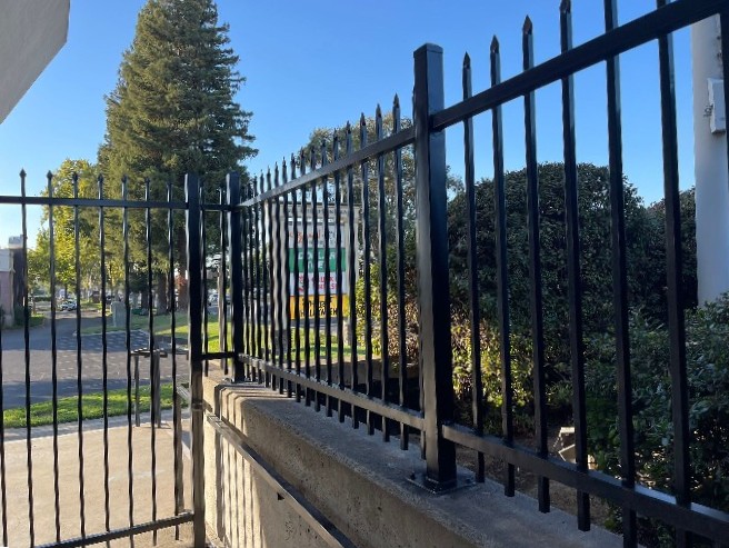 Spear-top ornamental iron pickets and welded panels in black powder coat on a concrete curb wall, Univision Sacramento