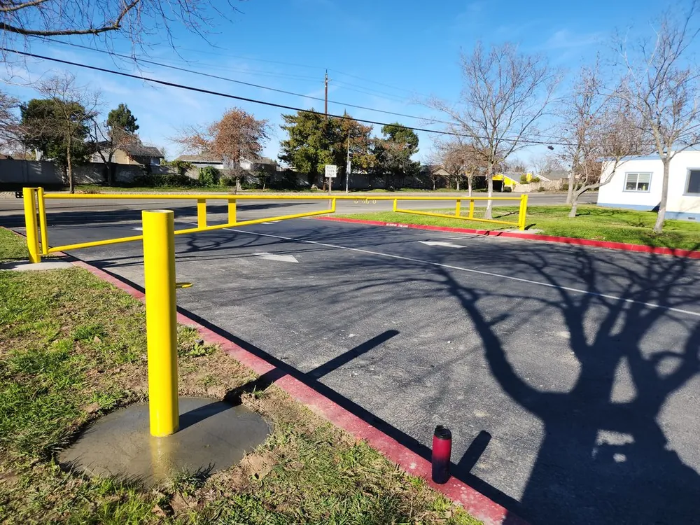 Yellow steel bollards and a barrier controlling a parking-lot entrance, installed by Palmer Fence near Sacramento