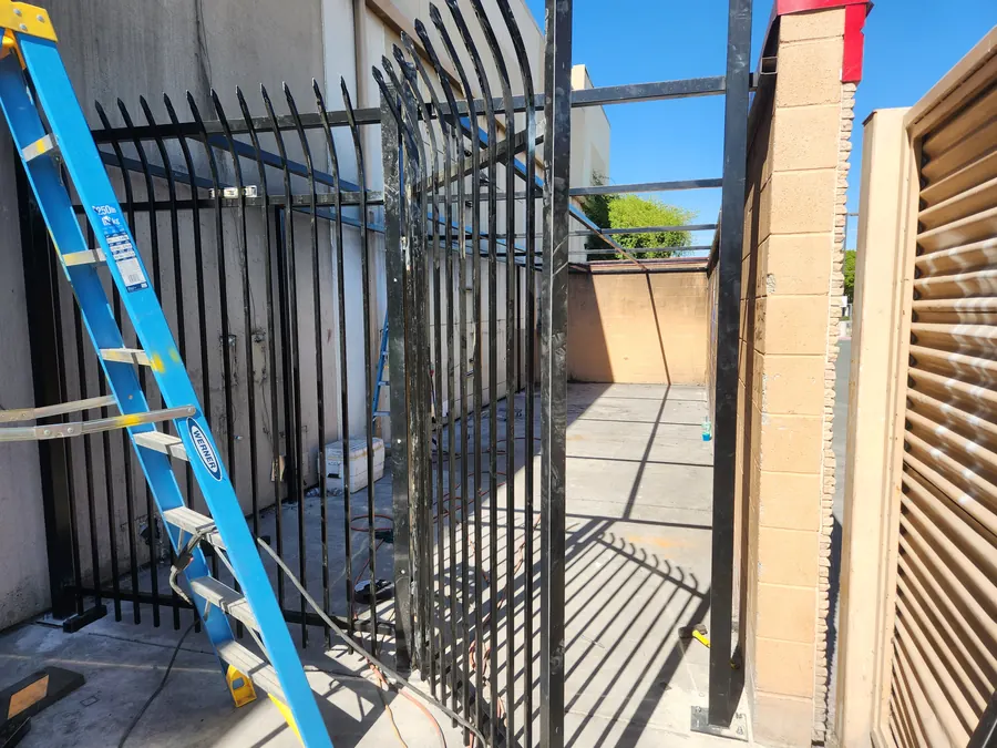 Palmer Fence crew mid-repair on curved-top steel security gate panels at a Sacramento commercial site