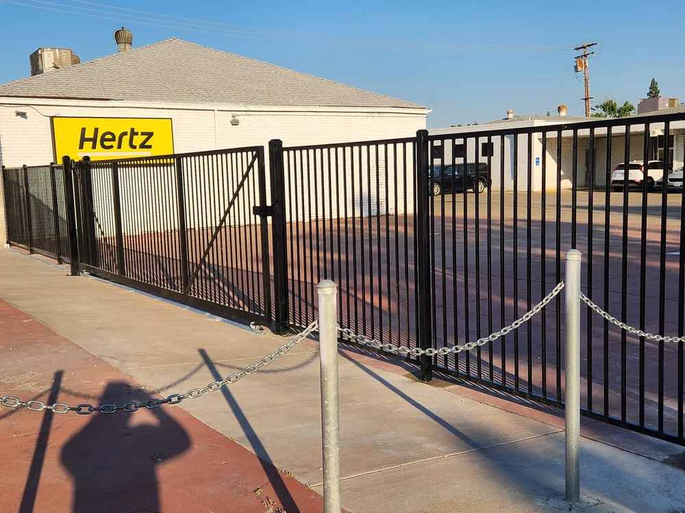 Black ornamental iron fence and walk gate at a rental car location, built by Palmer Fence