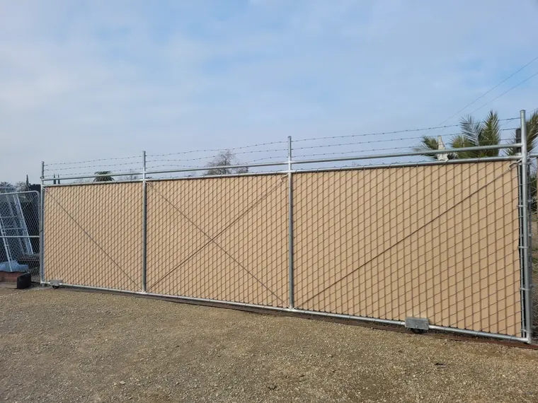 Galvanized chain link rolling gate with privacy slats and barbed wire, built by Palmer Fence