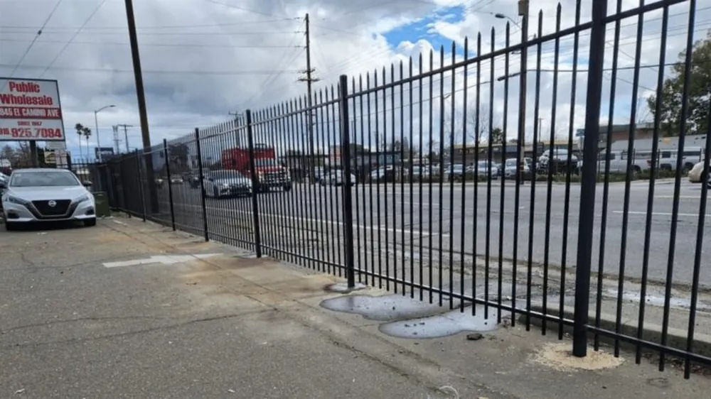 Repaired black ornamental iron fence at a Sacramento car lot, matched to the existing curve top line