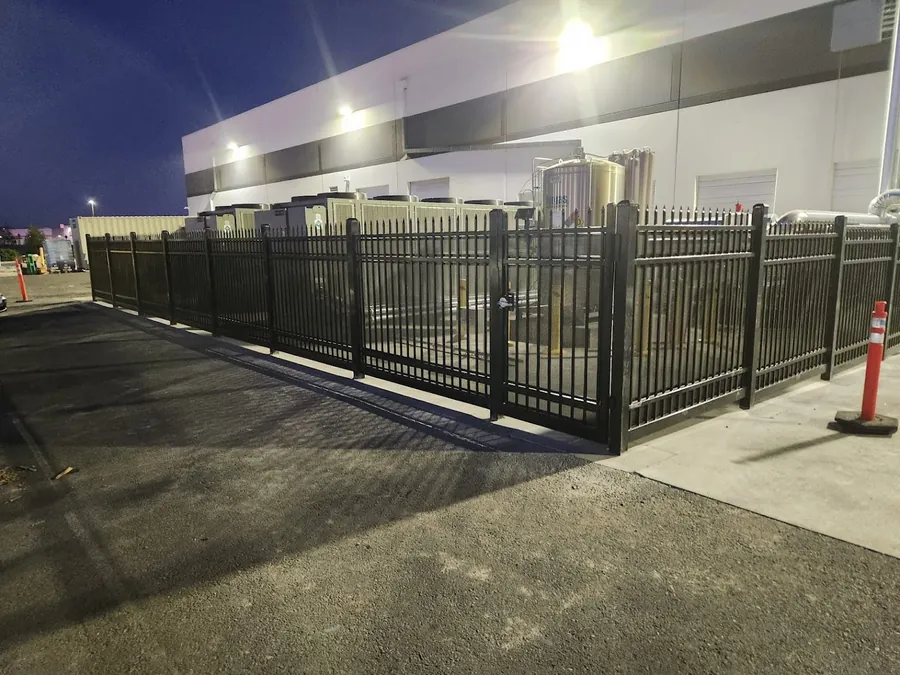 Black four-rail ornamental iron fence and pedestrian man gate at a Natomas commercial facility