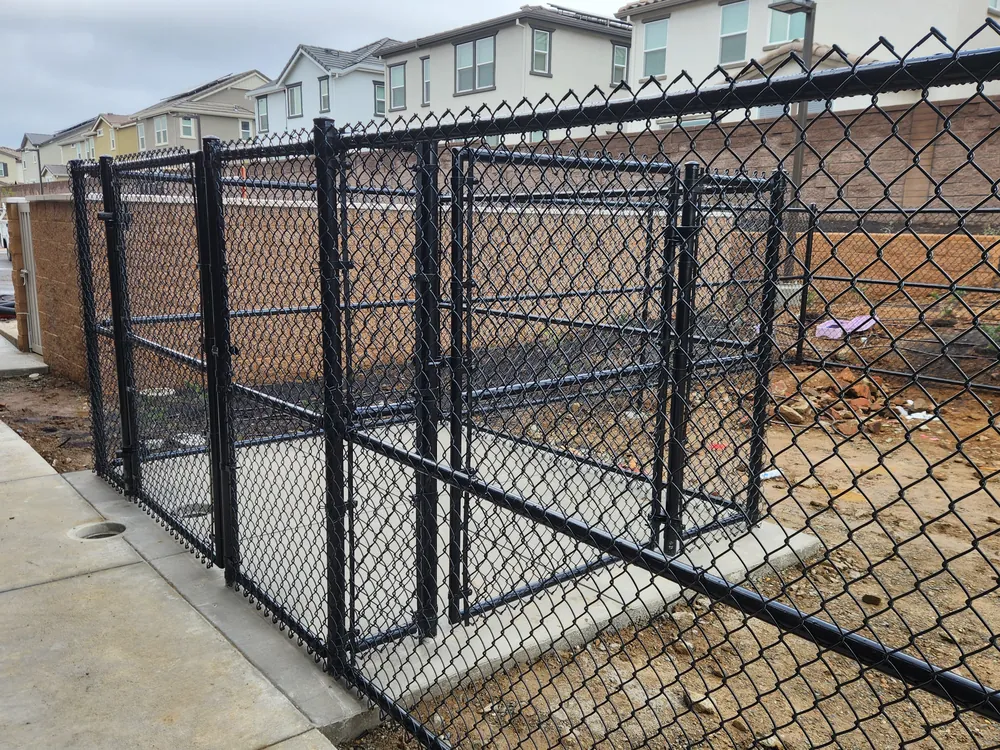 Black vinyl-coated chain link enclosure with double gates on a concrete pad at a new build, installed by Palmer Fence