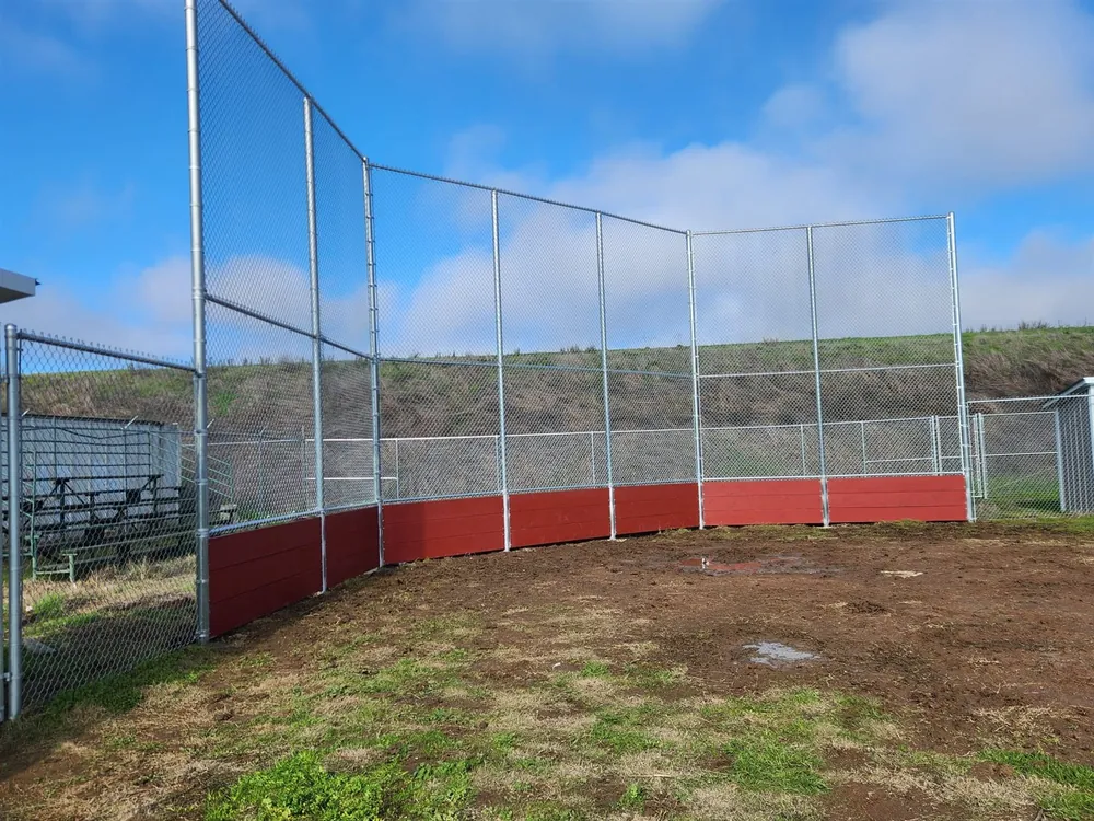 Tall galvanized chain link backstop with a red kick panel at a ball field, built by Palmer Fence