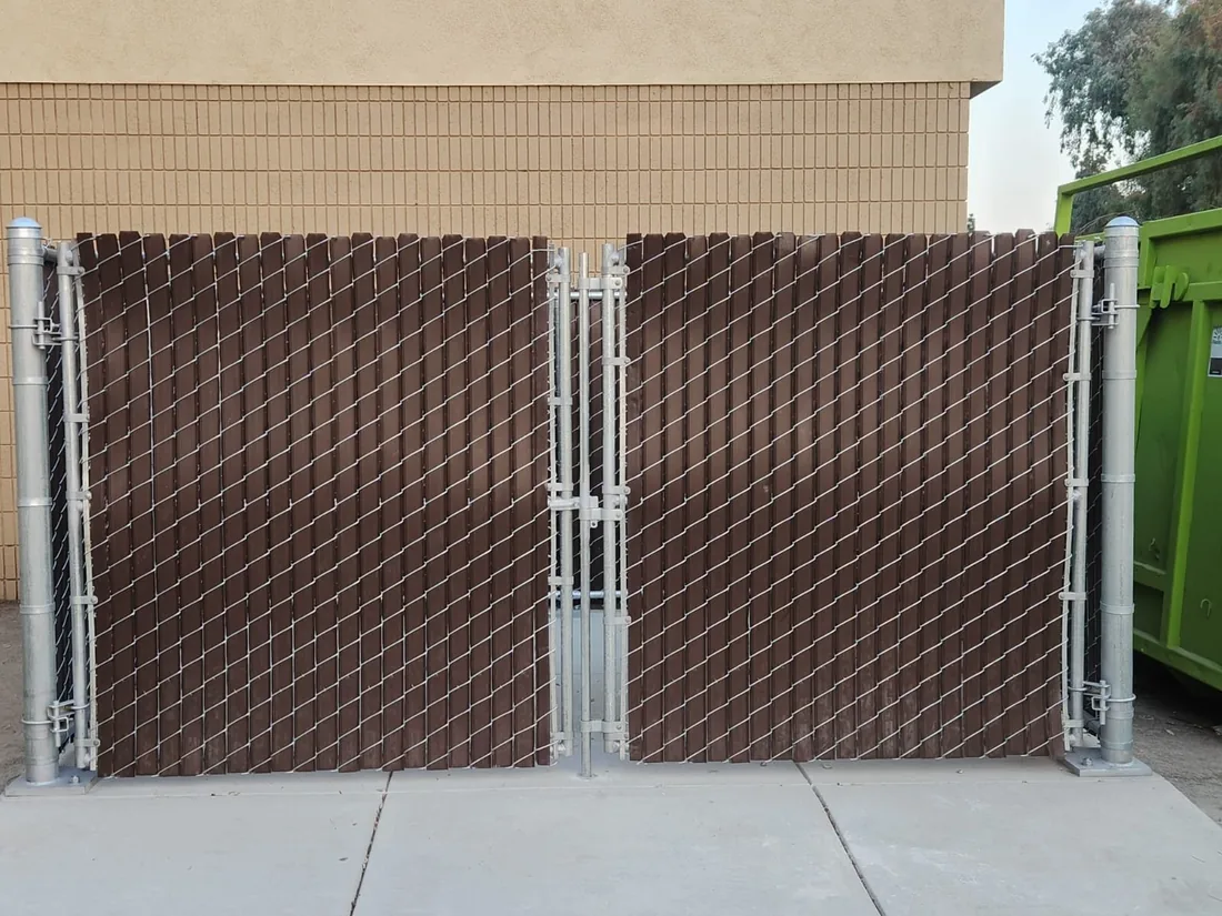 Chain link dumpster enclosure gates with brown privacy slats, built by Palmer Fence