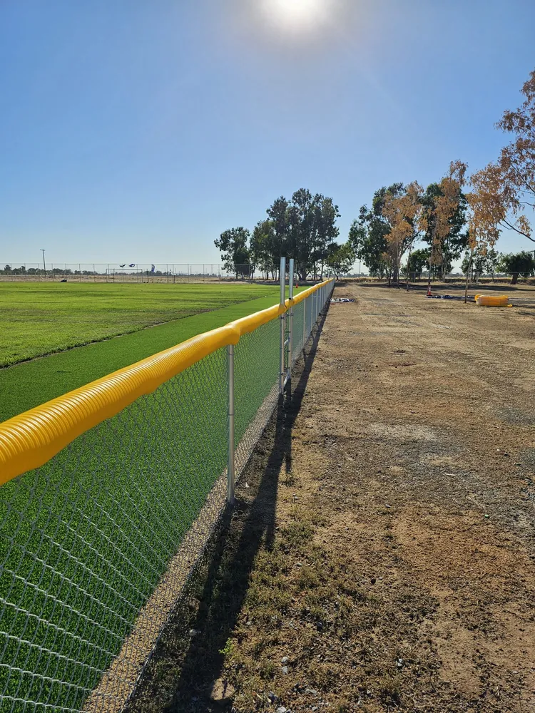 Galvanized chain link fence along a turf field with a yellow safety cap over the top rail, installed by Palmer Fence