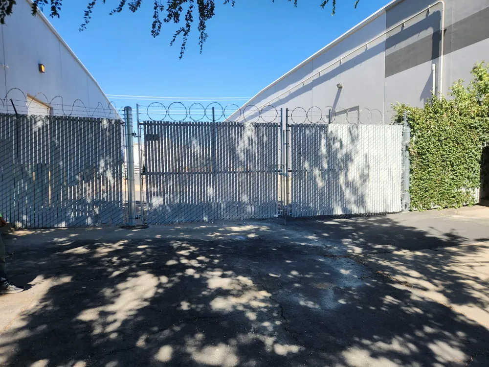 Chain link gates with grey privacy slats and razor wire above barbed wire between two warehouse buildings, built by Palmer Fence