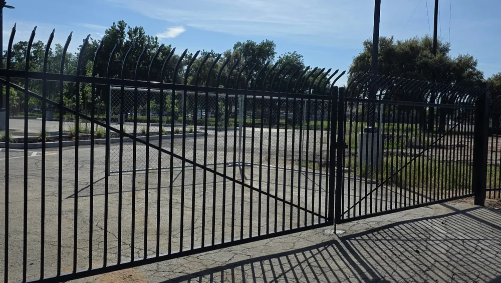 Black double swing gate with curved security pickets closing a commercial lot entrance, built by Palmer Fence in Sacramento