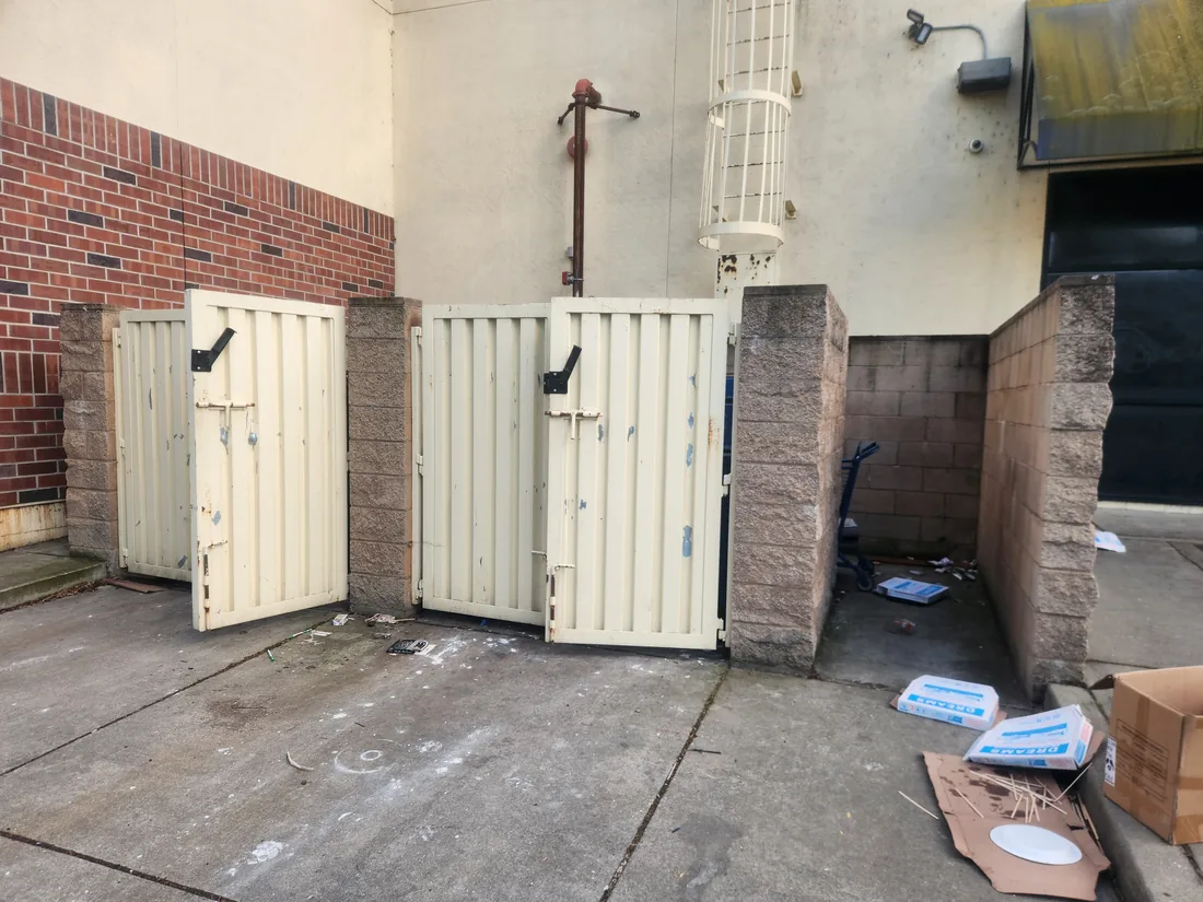 Commercial dumpster enclosure before Palmer Fence added the security fence, worn gates and an open top