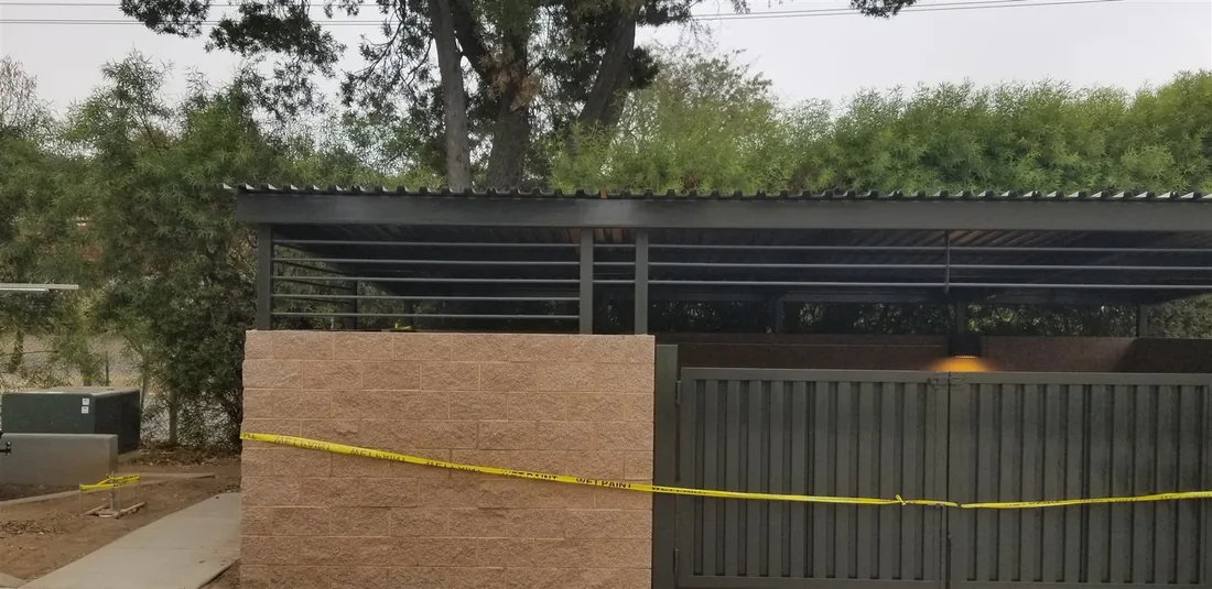 Metal roof on a steel frame over a block wall dumpster enclosure, built by Palmer Fence