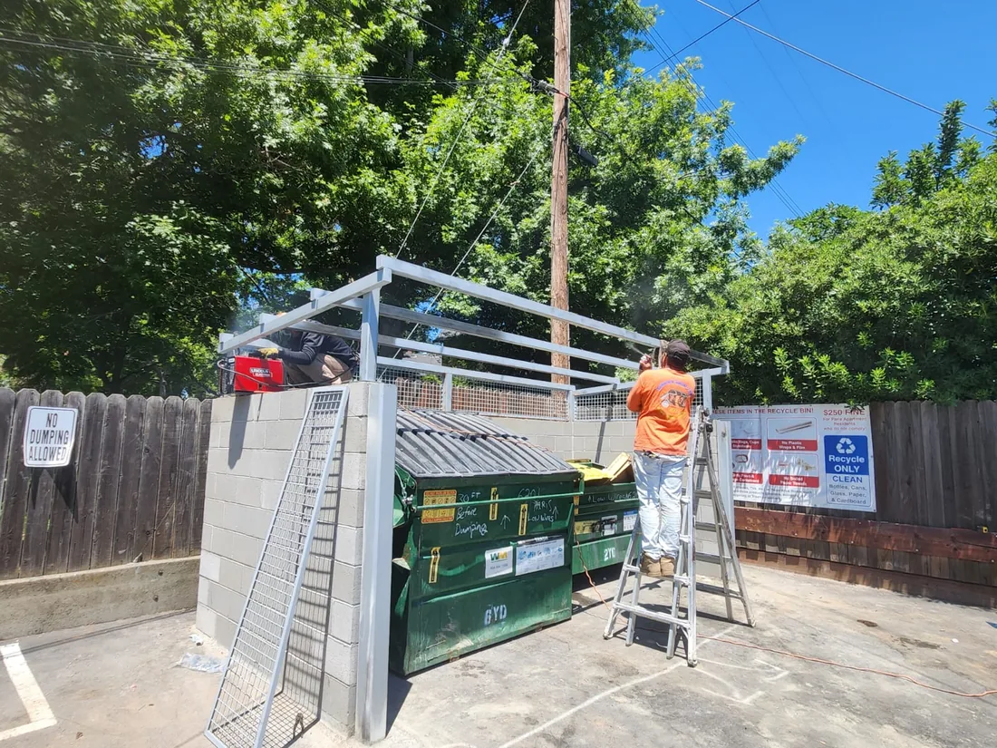 Palmer Fence crew welding the steel roof frame on a block wall dumpster enclosure in Sacramento