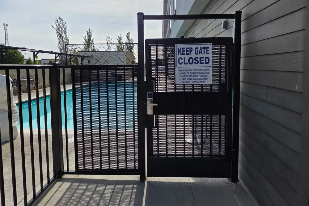 Black expanded metal pool gate with a self-closing latch at a commercial pool deck, built by Palmer Fence