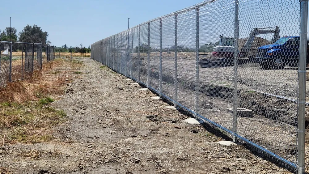 Long galvanized commercial chain link perimeter running along a jobsite, installed by Palmer Fence