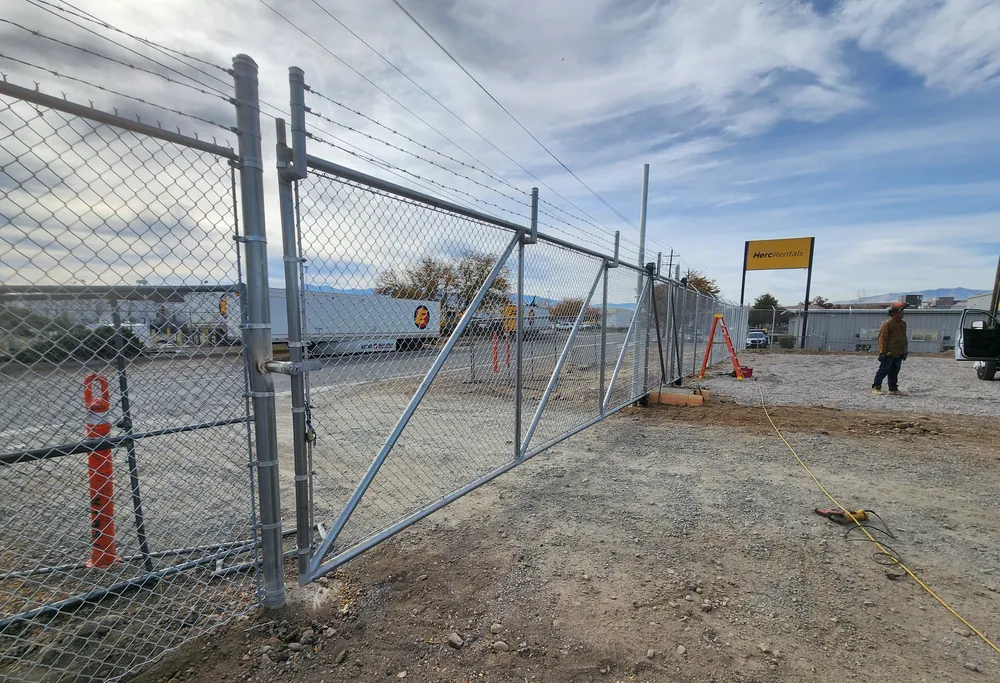 Galvanized chain link rolling gate with three-strand barbed wire at an equipment rental yard, installed by Palmer Fence
