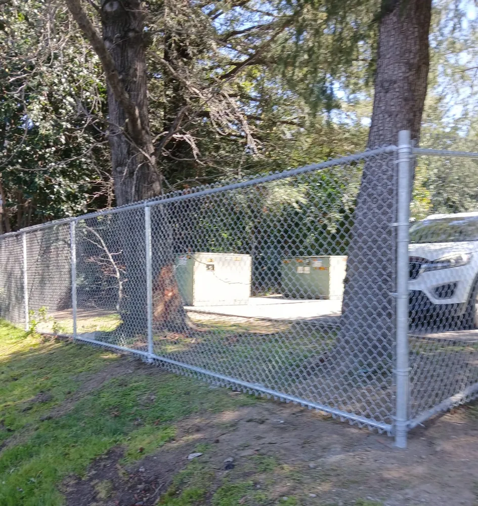 Galvanized chain link enclosure around utility equipment cabinets under trees, built by Palmer Fence