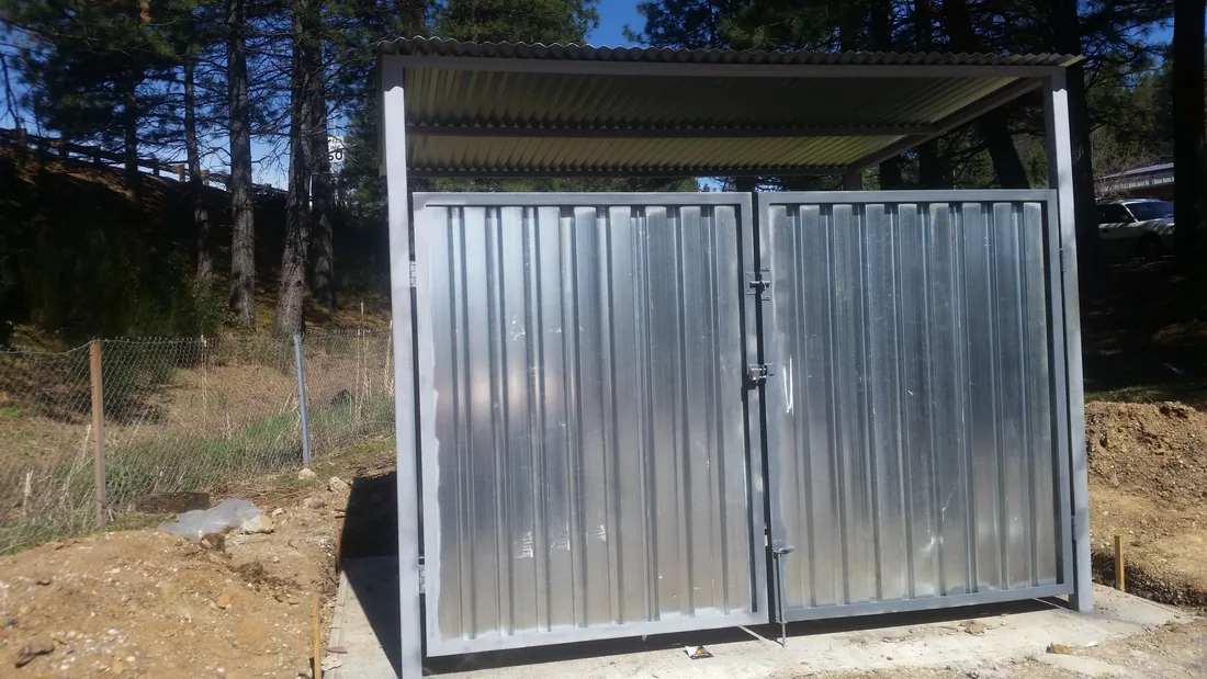 Galvanized corrugated dumpster enclosure with a metal roof on a new build, by Palmer Fence
