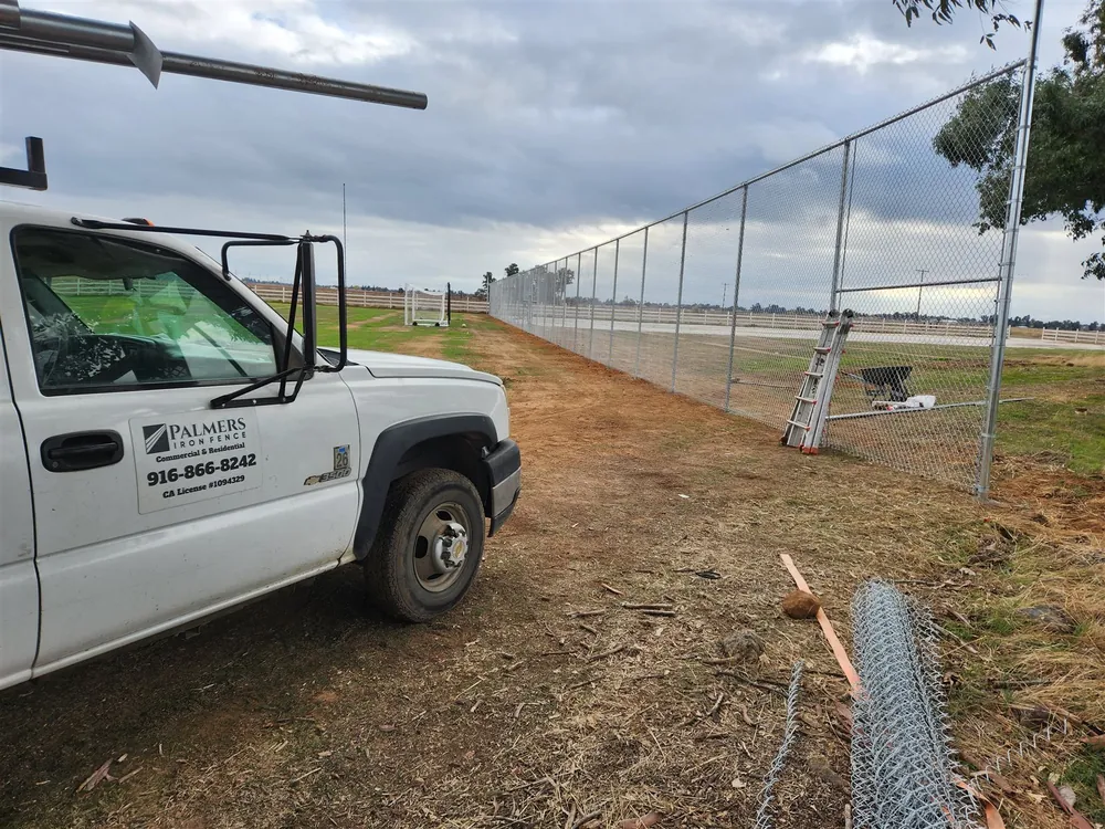 Palmer Fence truck parked along a long galvanized chain link run under construction at a sports complex