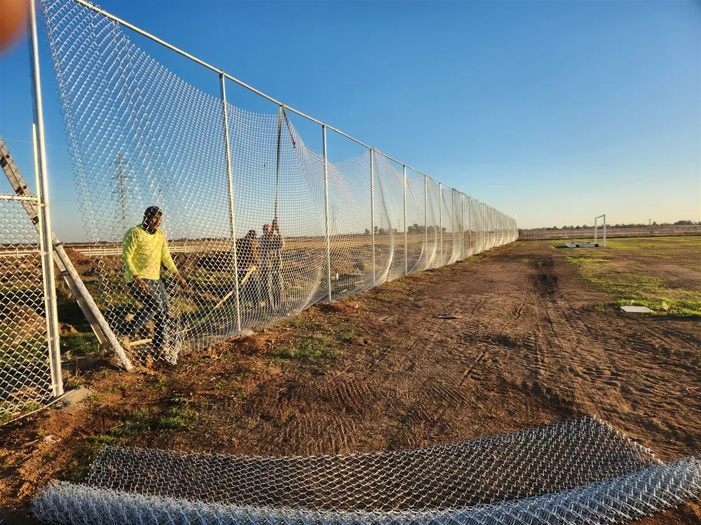 Palmer Fence crew stretching fabric on a tall galvanized chain link run at a sports field