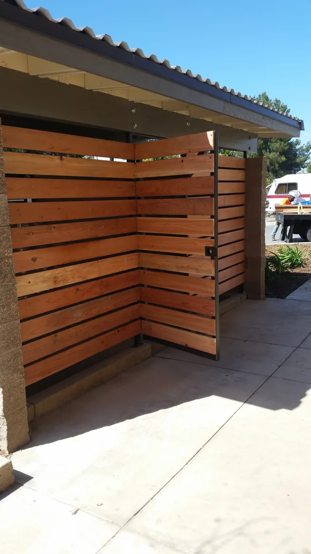 Redwood slat screen on a steel frame under a metal roof at a commercial enclosure, by Palmer Fence