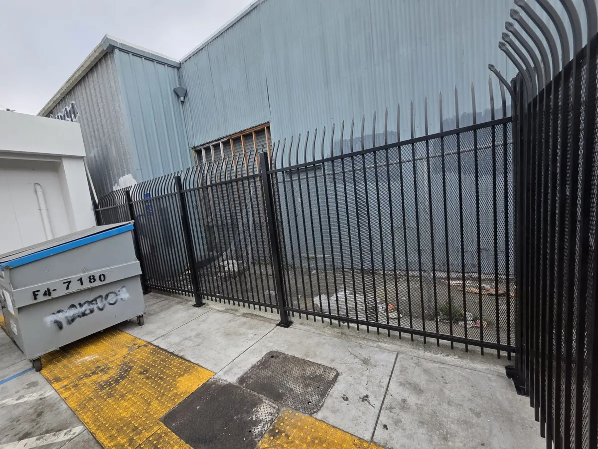 Black curved-top steel security fence with expanded metal behind the pickets around a commercial lot