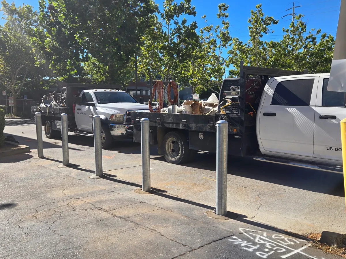 Row of galvanized steel bollards along a parking lot, some of them removable with a chain attached